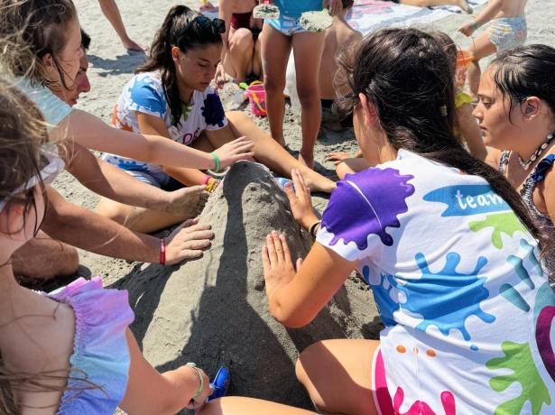 Bambini costruiscono una scultura di sabbia in spiaggia sotto gli ombrelloni colorati.